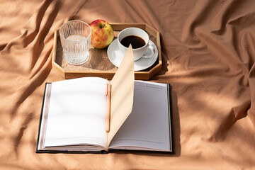 Open notebook and coffee cup on tray. Cozy morning at bed.