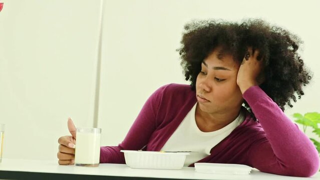 African American teenage girl tired of eating unsatisfying, unhealthy boxed meals. Sitting and staring at bland boxed food, using a spoon to dig into the nutritious rice.