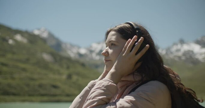 Woman with dark hair and black headphones enjoying music in the mountains