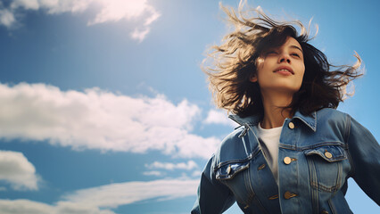 Happy and beautiful young caucasion woman wearing denim jacket enjoys sunny summer day smiling with flying hair, sunshine, blue skies, white clouds, low angle shot, copy space, 16:9  - obrazy, fototapety, plakaty