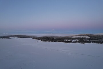 Moon rises over a tranquil, snowy expanse in the fading Arctic light.
