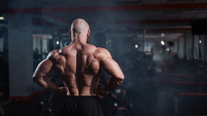 Fototapeta na wymiar Muscular bald man posing shirtless. Bodybuilder demonstrating back muscles in the gym.