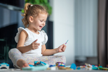 Happy little girl playing with small constructor toy on floor in home, educational game, spending leisure activities time concept