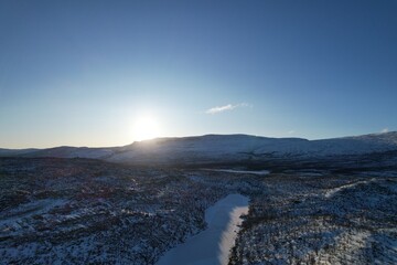 The early morning sun illuminates the rugged terrain of Stenbacken, revealing a vast expanse of snow and scattered evergreen trees.