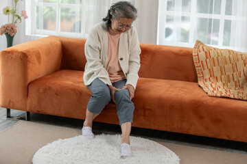 Asian old woman with his knee joint pain in sofa, pain in the elderly, health care, elderly care. Elderly man having a knee pain and sitting down. Grandmother with knee pain.