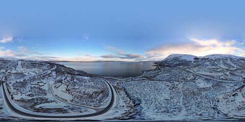 A panoramic drone shot captures the tranquil twilight of Björkliden, with curving roads embracing...