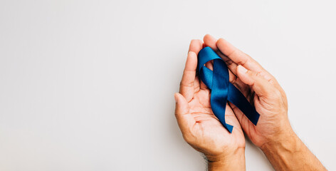 Supporting men's health awareness in November, hands hold a blue ribbon, emphasizing the importance...