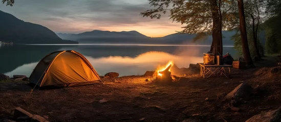 Fotobehang camping with a tent on the lake bank in early morning. morning sunlight touches against forest hill © Beny