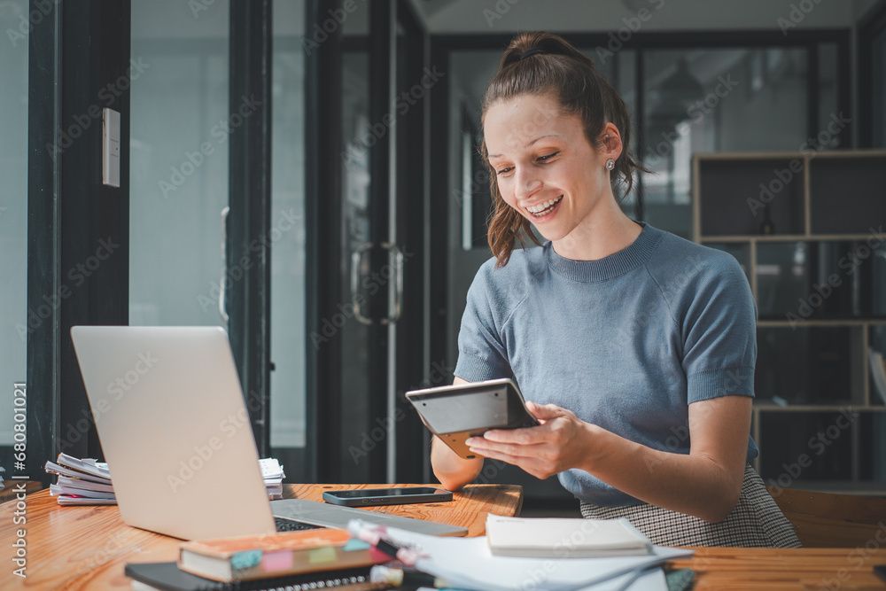 Poster smiling young woman using calculator and laptop computer to calculate financial report, working at o