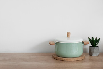 Fototapeta na wymiar Green cooking pot and houseplant on wooden kitchen counter