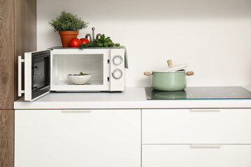 Modern microwave oven with food and cooking pot on white kitchen counter - obrazy, fototapety, plakaty