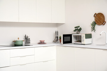 Interior of light kitchen with microwave oven, electric stove and utensils on white counters