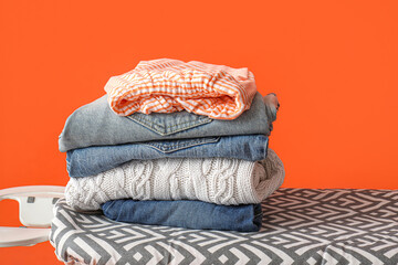 Stack of clean clothes on ironing board against orange background, closeup