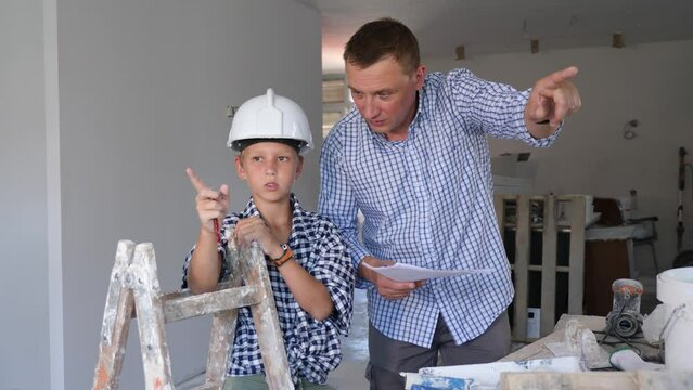Friendly adult man with construction documents talking with preteen son and gesturing inside apartment being renovated