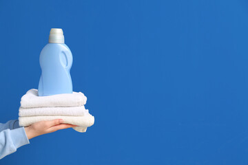 Female hands holding stack of clean towels with laundry detergent bottle on blue background