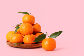 Wooden plate with sweet mandarins on pink background