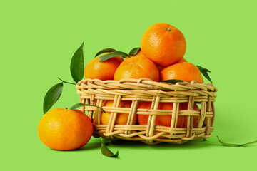 Wicker bowl with sweet mandarins and leaves on green background