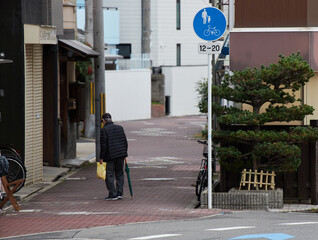 冬の朝の住宅街の道路で歩く一人のシニア男性の姿