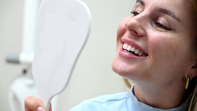 Young Beautiful woman smile after Dental Whitening process smile in mirror. Teeth whitening with UF Lamp, Led Lamp and gel in Dental Clinic. 4k 120 fps slow motion Raw footage