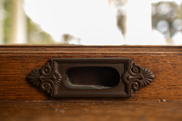 Closeup of an ornate bronze handle on the wooden frame of a window in a historic mansion.