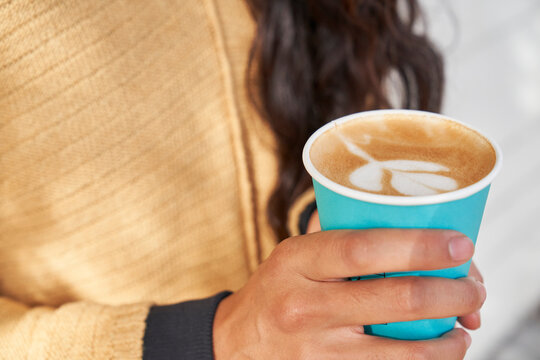 Woman with latte in blue paper cup hand and latte art