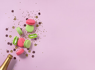 Creative Christmas and New Year composition with golden champagne bottle, confetti, pink and green macarons, copy space. Flat lay.