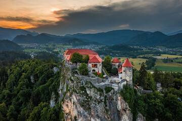 Bled, Slovenia - Aerial view of beautiful Bled Castle (Blejski Grad) with dramatic golden sunset sky over Julian Alps at background
