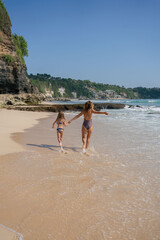 Beautiful little girl enjoying with her mother on the beach. They are running on the seashore and having fun. High quality photo