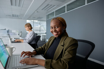 Two young multiracial businesswoman in businesswear smiling and typing on laptops at desk in office