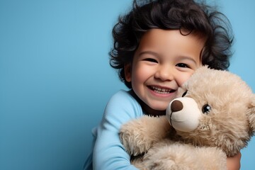 Adorable Fictional Little Child in Plain Casual Shirt Holding a Teddy Bear and Smiling. Isolated on a plain blue background. Generative AI.