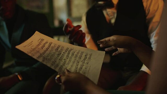 Cropped shot of African American female jazz vocalist with piece of sheet music in hands discussing lyrics and melody with band members during concert rehearsal in jazz club