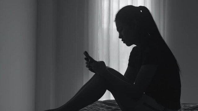 Silhouette of woman with depression and depression sitting using smartphone in room, Sad, Anxiety, Family Problems, Mentally ill Person, Domestic Violence