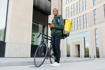 The pizza delivery man next to the bicycle looks at the delivery address on the phone outside....