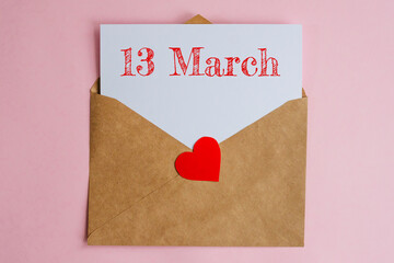 Kraft envelope with a white sheet of paper and a date 13 march, with a red heart. Flat lay on pink background, romance and love concept