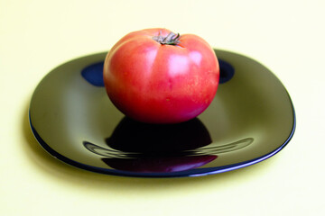 Big red tomato on a black plate close-up. Agriculture concept