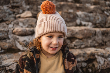 close up portrait of little fashionable boy with hat in earth tones, medieval stone castle...
