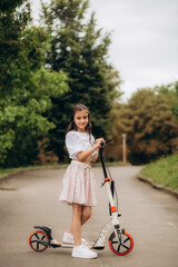 Fototapeta na wymiar Little girl riding a kick scooter on a street near home