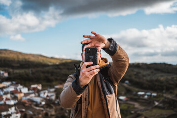 Young happy photographer man traveling sightseeing in a small town, taking a photo with his cell...