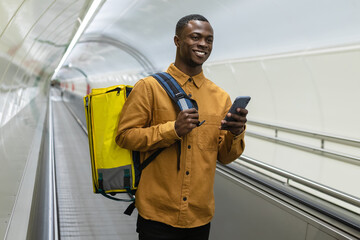 A smiling pizza delivery man with a mobile phone in his hands. The courier in the subway crossing goes to the customer