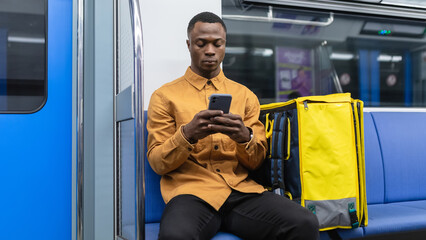 An African-American delivery man spends time on his mobile phone while riding the subway. Professional delivery from the restaurant