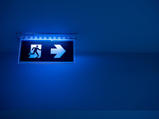 Blue tone of LED light fire escape sign hang on the ceiling in the dark building. Emergency fire exit sign, warning plate with running man icon and arrow to the right way with copy space.
