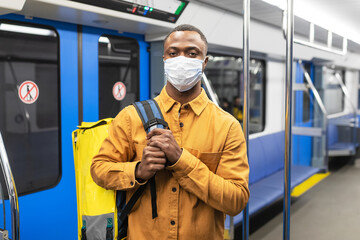 Portrait of a male courier in a protective mask on public transport. Food delivery during a pandemic