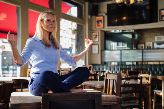 Blond businesswoman sitting and doing yoga on table in coffee shop