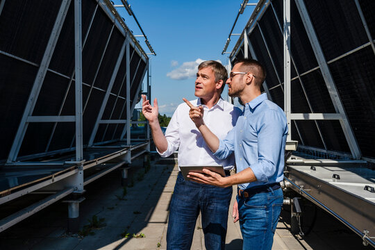 Two businessmen discussing on rooftop beside refrigeration installation