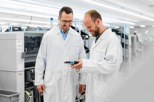 Technicians in white lab cots disussing over electronic component