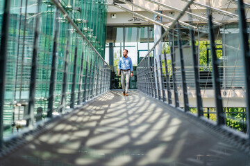 Businessman walking in corridor of modern office building carrying digital tablet