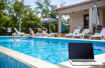 Laptop with blank screen kept near swimming pool on sunny day