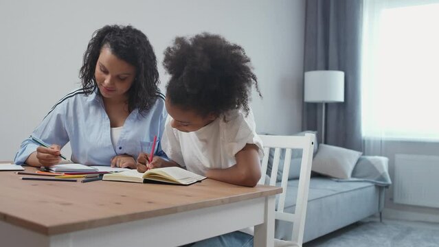 Handheld, pretty dark-skinned girl doing homework at home with her mom, draw lessons, homeschooling.