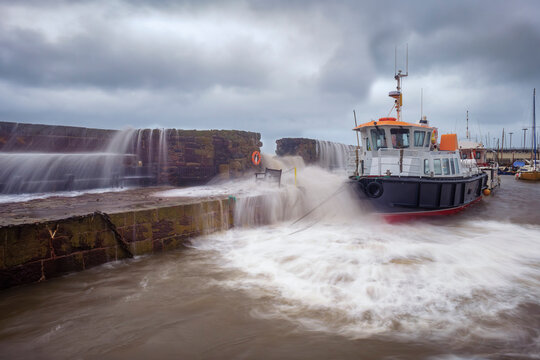UK, Scotland, North Berwick, Long exposure of waves breaking over harbor wall in front of moored boat