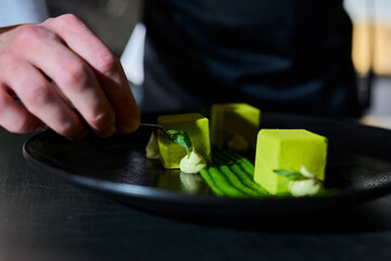 Close-up of the pastry chef's hand with tweezers that decorates the dessert with greenery. Haute cuisine. Beautiful serving of dishes